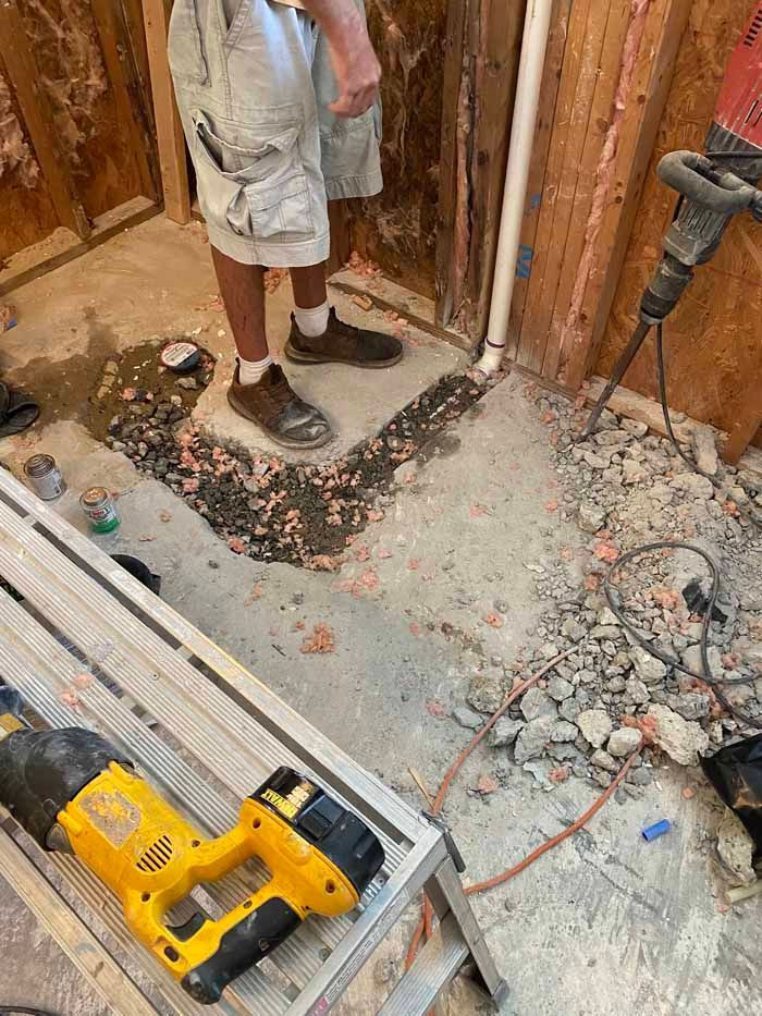 Person standing on a partially demolished floor with a yellow power drill in a construction area