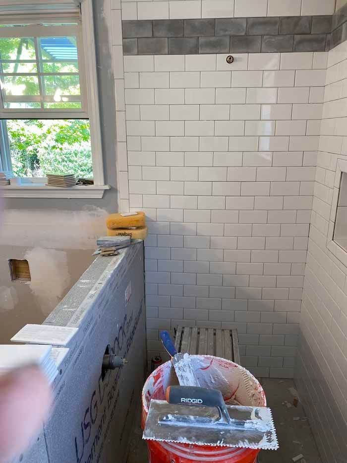 Bathroom under renovation with white subway tile shower wall, window, and paint tools in the foreground