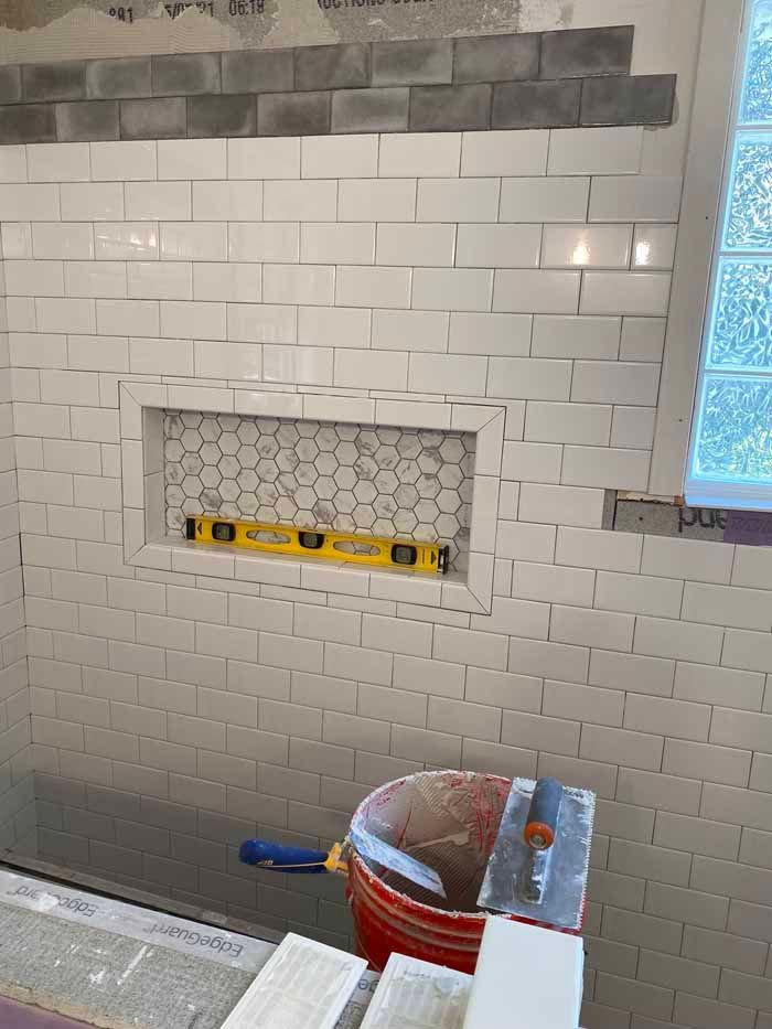 Bathroom shower wall with white subway tile, recessed niche, and tools on the floor during renovation