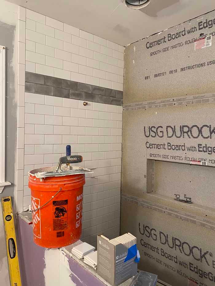 Small tiled shower under construction with orange bucket, tools, and USG Durock wall panels