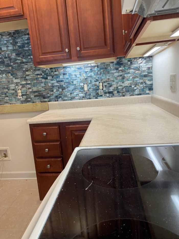 Modern kitchen with dark wood cabinets, light counters, and blue mosaic backsplash beside a stovetop.