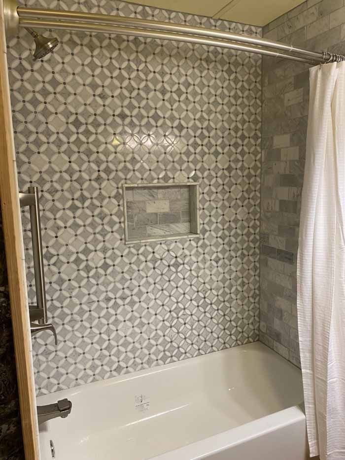 Bathtub with patterned tile shower wall, built-in niche, and white shower curtain.
