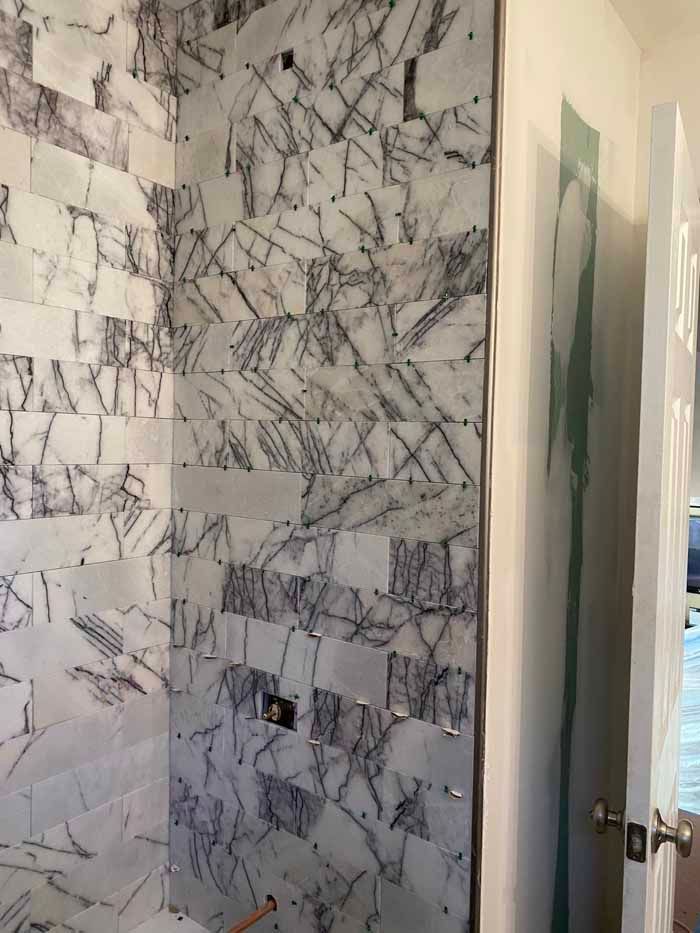 Marble-tiled bathroom shower wall with a recessed niche and open white door