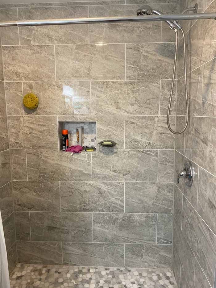 Tile-lined shower with a built-in niche, showerhead, and visible plumbing fixtures in a bathroom under renovation