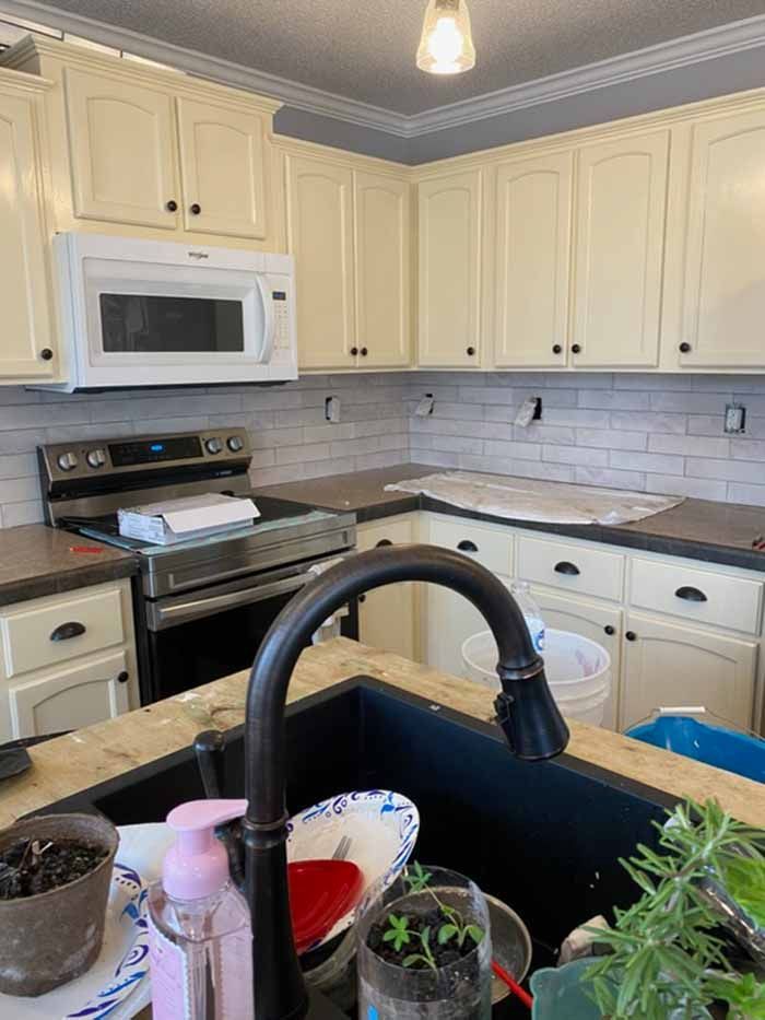 Bright kitchen with cream cabinets, white tile backsplash, black stove, and sink in foreground.