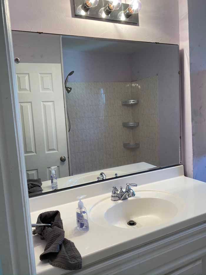 Bathroom vanity with large mirror, white sink, soap dispenser, and dark towels on the counter.