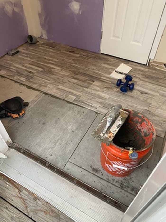 Partially tiled floor under renovation with tools, bucket, and unfinished purple wall near a door