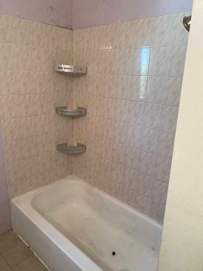 White tiled shower/tub corner with built-in shelves and a small bathtub