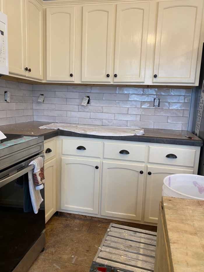 Small kitchen with white cabinets, gray tile backsplash, and a black stove beside a countertop.
