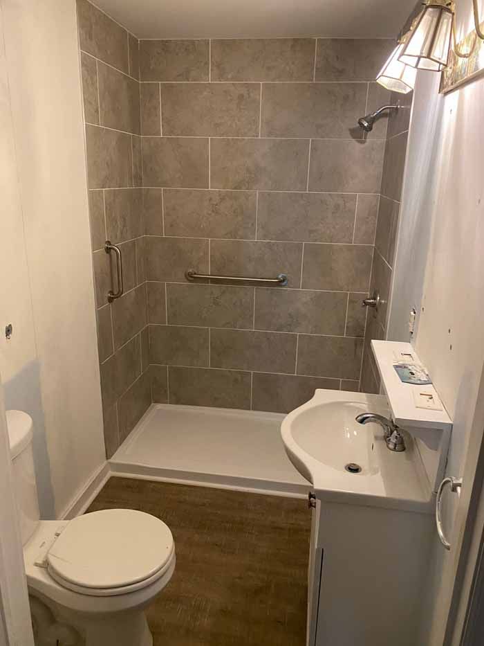 Small bathroom with a toilet, sink vanity, and walk-in shower with grab bars.