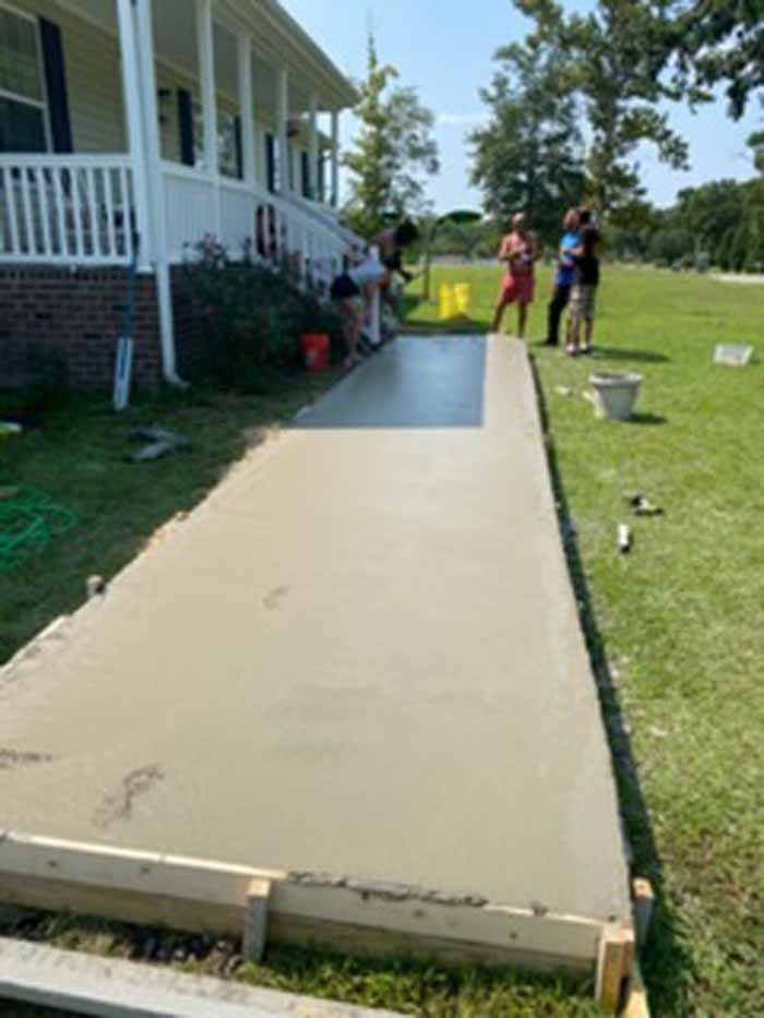 Freshly poured concrete walkway alongside a house, with people standing at the far end.