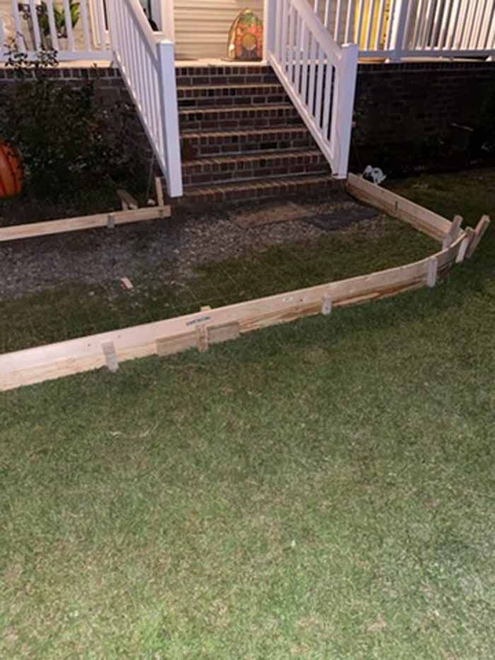 Bent wooden barrier in a front yard beside porch steps at dusk