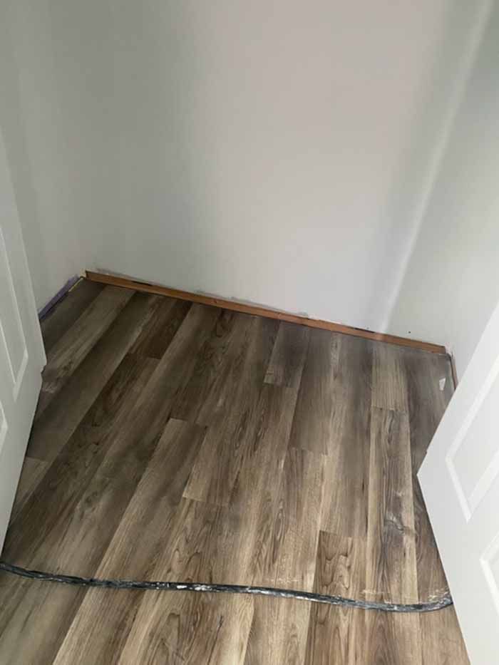 Small empty closet with wood-look flooring and white walls, viewed through an open doorway