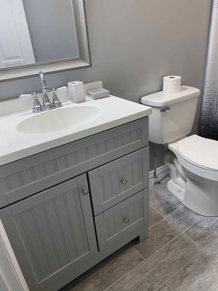 Modern bathroom with gray vanity, white sink, toilet, mirror, and gray wood-look flooring