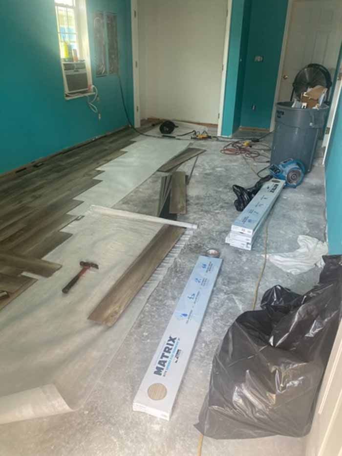Room under renovation with teal walls, floorboards, tools, and construction debris scattered on the floor