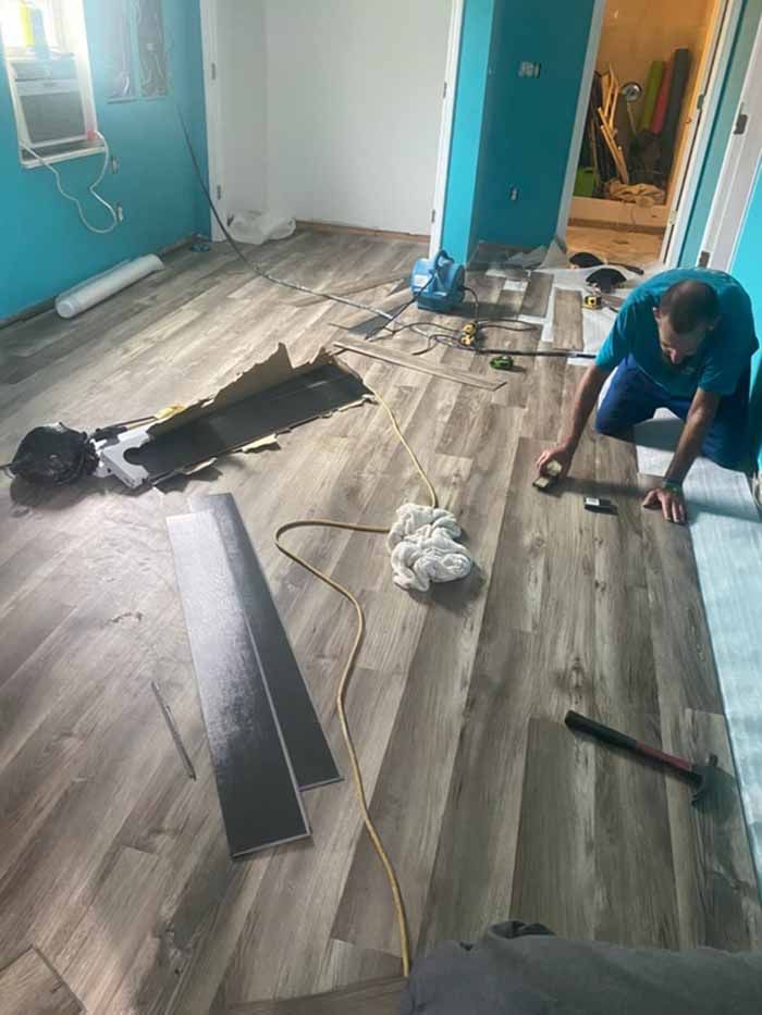 Person installing wood flooring in a room with teal walls and scattered tools and planks
