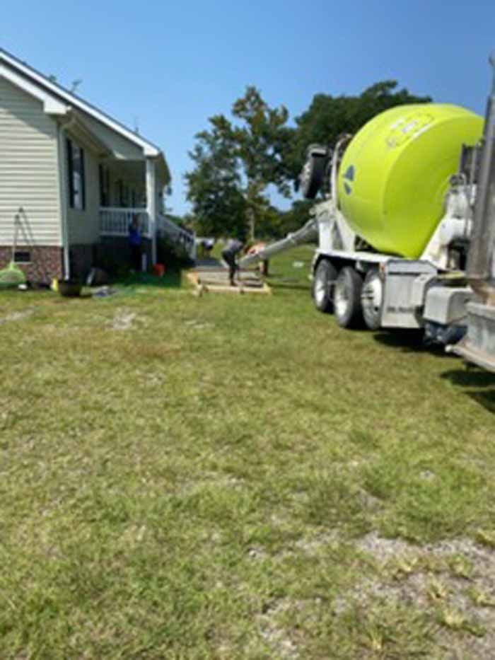 Concrete truck and worker beside a house on a sunny lawn, with a bright green mixer drum.