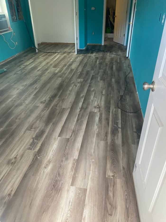 Empty room with gray wood flooring, turquoise walls, and a white door partly open.