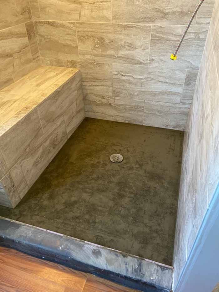 Walk-in stone shower with bench, tiled walls, and a concrete floor with a drain.