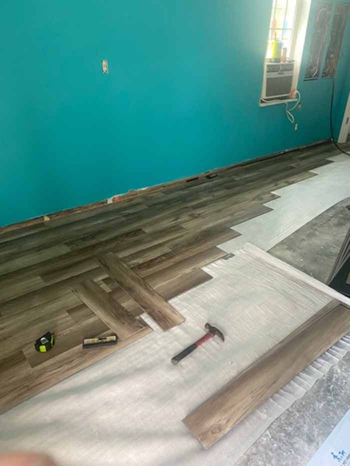 Partially installed gray herringbone flooring in a teal-walled room, with tools on the floor.