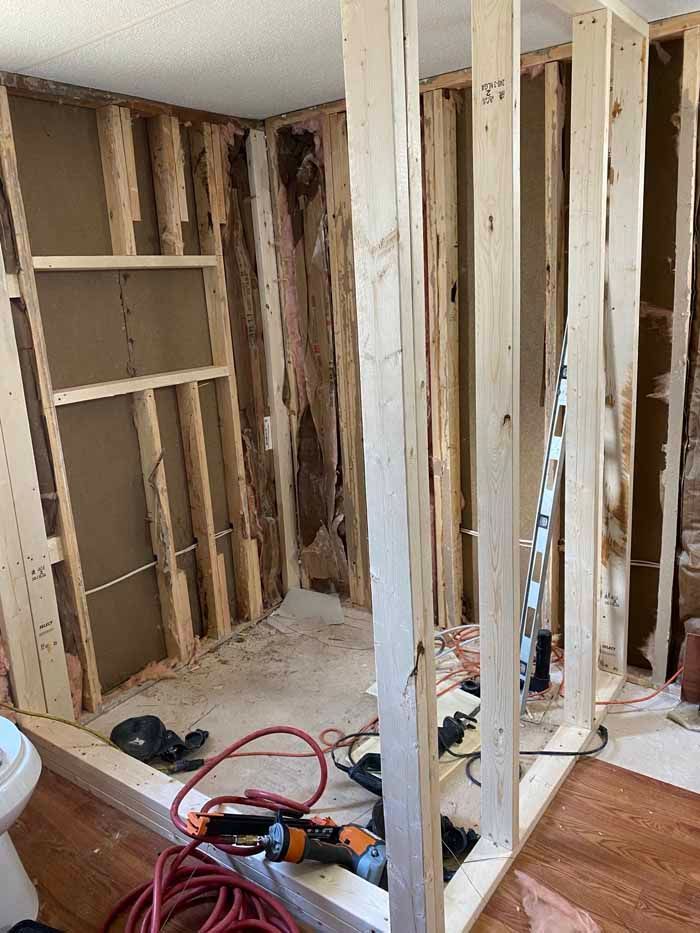 Partially gutted room with exposed wall studs, tools, and construction debris on the floor