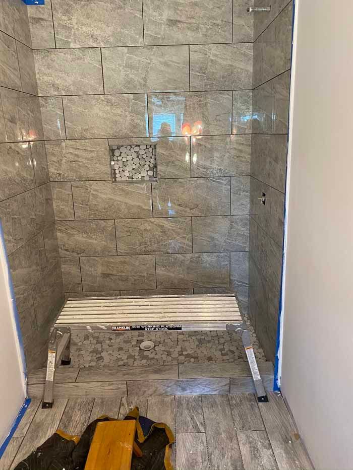 Tiled shower under construction with bench, drain grate, and tools on the floor