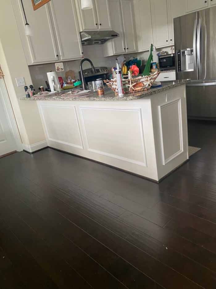 Modern kitchen with white cabinets, dark wood floor, and cluttered countertop beside a stainless steel fridge