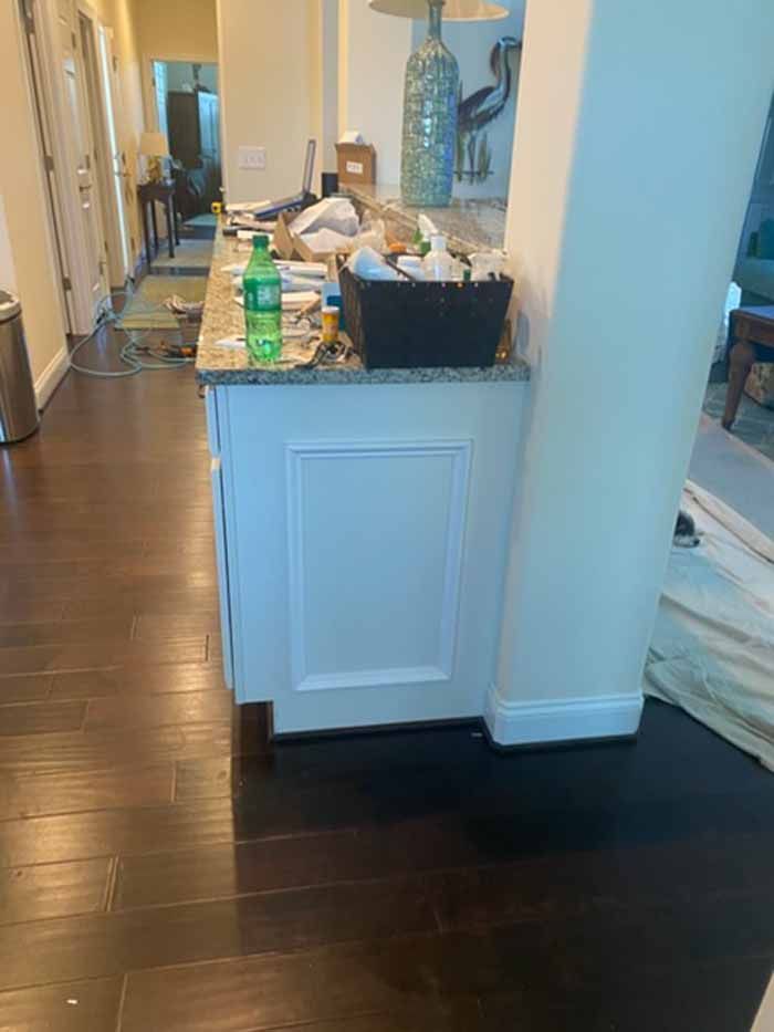 Kitchen island with groceries and dishes in a hallway, beside a bedroom with unmade bed.