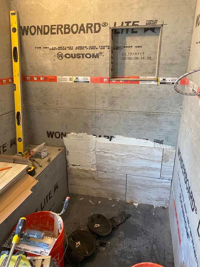 Partially tiled shower under renovation with WonderBoard walls, tools, and construction materials