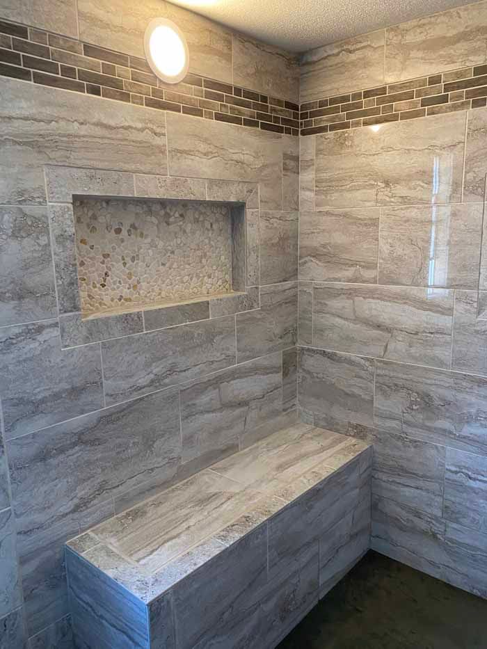 Stone-tiled shower with built-in bench and recessed shelf under a wall light