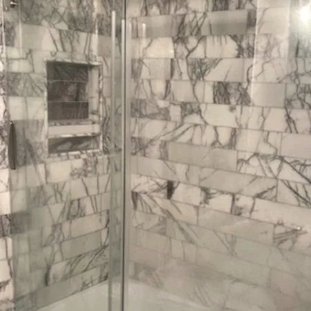 Marble-tiled shower with a built-in niche and a glass partition