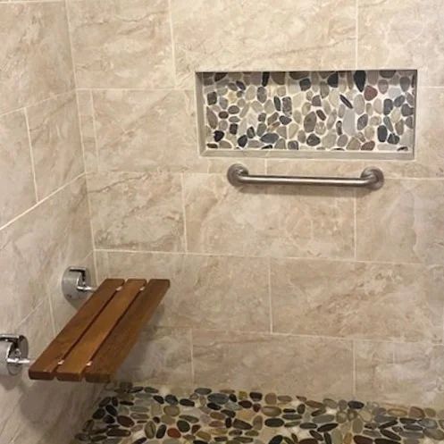 Accessible shower with beige tile, mosaic accents, grab bars, and a wooden folding seat