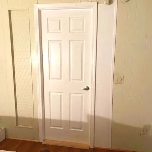 White interior door in a beige room with wood floor and a wall mirror on the left.