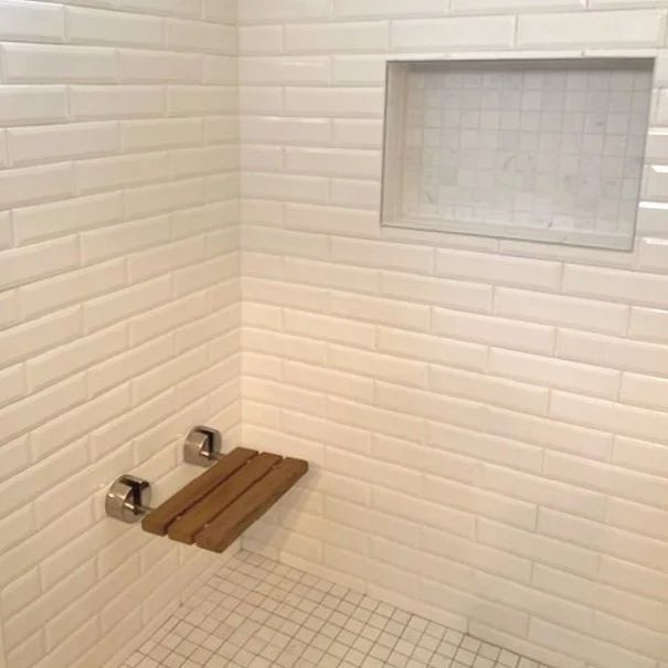 Small white-tiled shower with a built-in niche and a wooden bench seat.