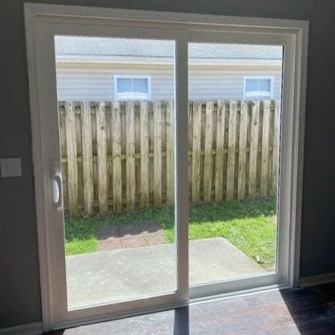 Sliding glass door opening to a small patio with a wooden fence and grass outside