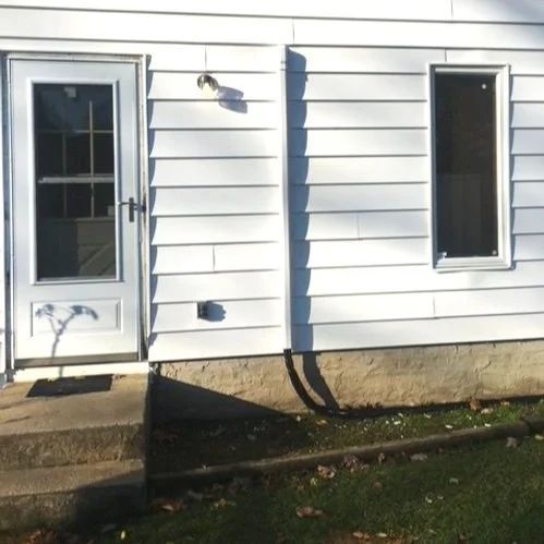 White house exterior with a glass door, narrow window, and concrete steps in front.