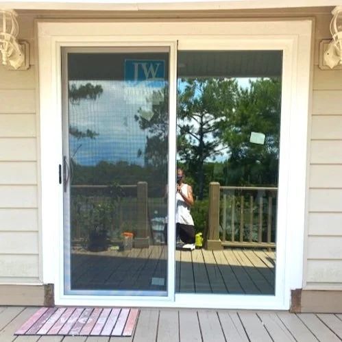Sliding glass door on a deck, reflecting trees and a person standing outside.