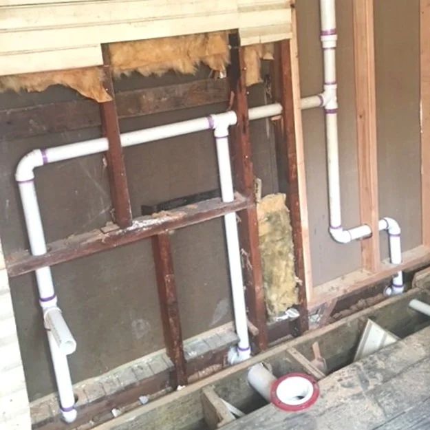 Exposed wall framing with white PVC pipes and insulation during renovation.