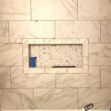 Built-in stone shower niche with a blue bottle, soap dish, and hex tile backing