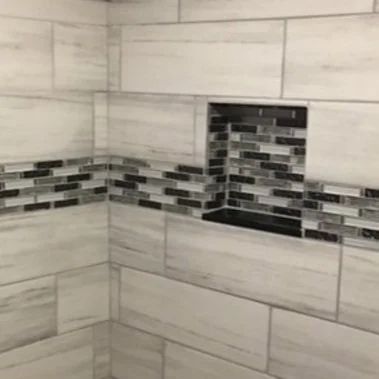 Tiled shower wall with gray stone-look tiles and a black, white, and gray mosaic accent strip