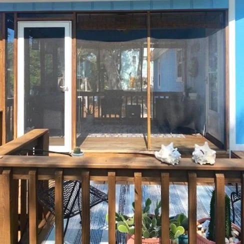 Wooden deck with potted plants facing a screened patio door and reflective glass wall