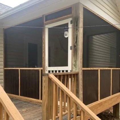 Covered wooden porch with screened walls, railing, and stairs on a house exterior.