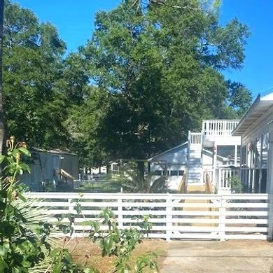 White slatted fence and backyard with trees, house deck, and clear blue sky.