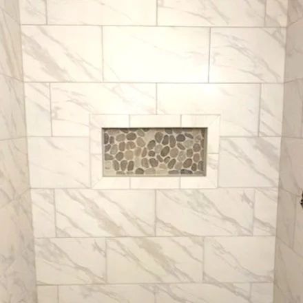 White marble-tiled shower wall with a small horizontal pebble-stone inset niche.