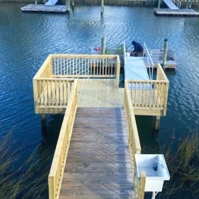 Wooden dock leading to a small waterfront platform with railings over blue water, with a person at the end