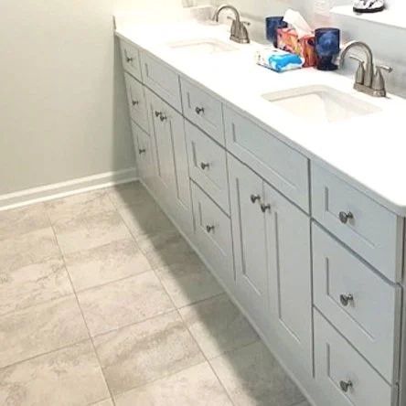 Long bathroom vanity with double sinks, white countertop, and gray cabinets on tiled floor.