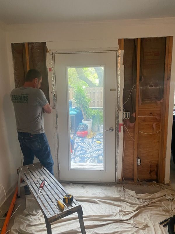 Worker installing a white glass door in a room under renovation, with tools and protective floor covering