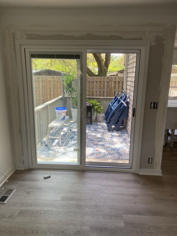 Empty room with sliding glass door opening to a fenced patio with stacked outdoor chairs and a tree.