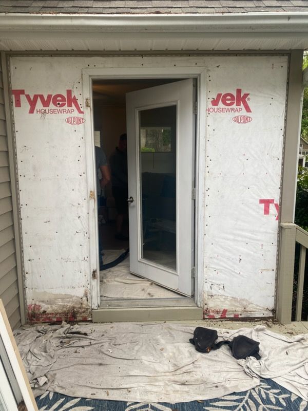 Tyvek-wrapped exterior doorway with a partially open door and debris-covered ground after renovation work