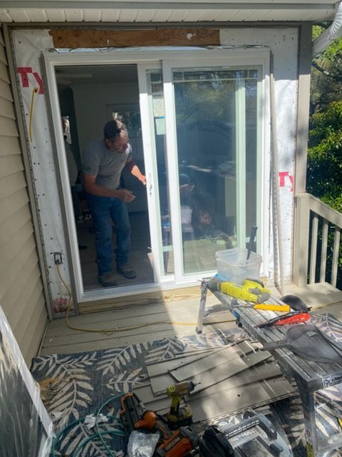 Worker installing a sliding glass door on a balcony, with tools and construction materials nearby.